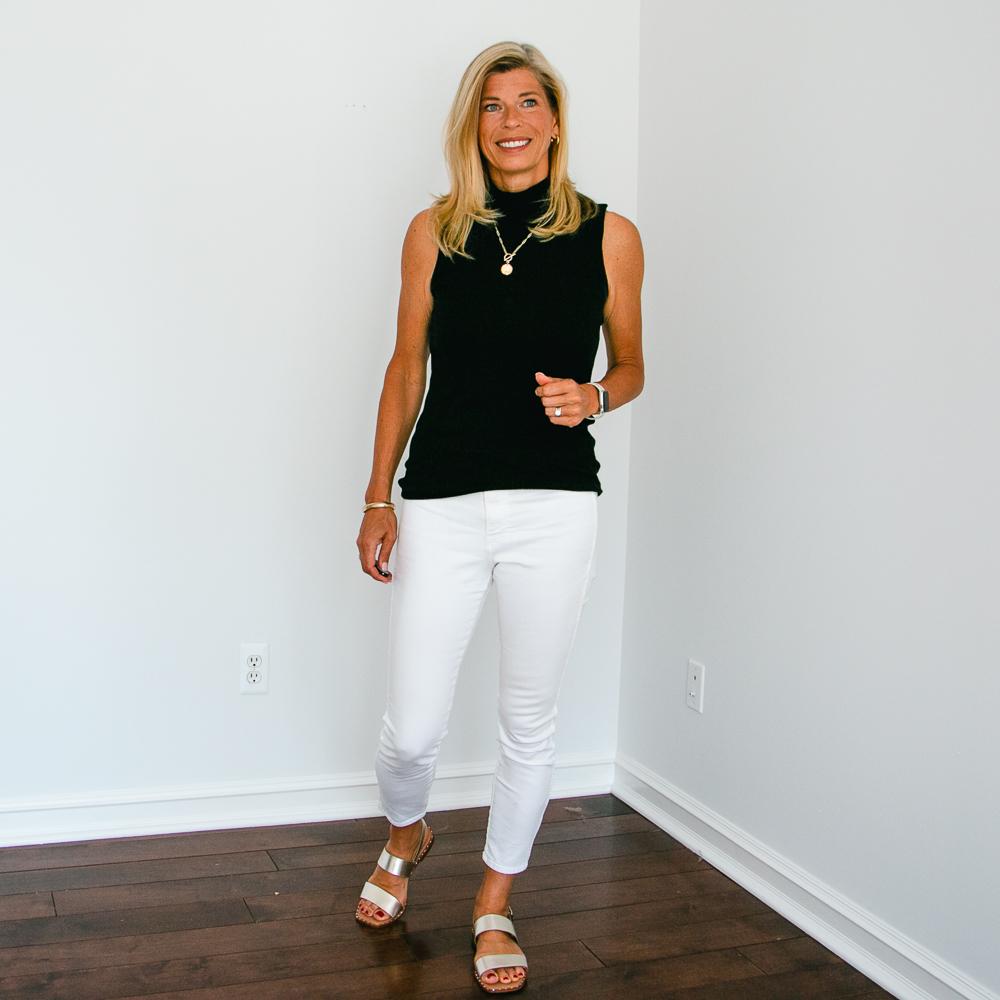 Black sleeveless turtleneck & white tapered jeans with gold sandals and accessories outfit